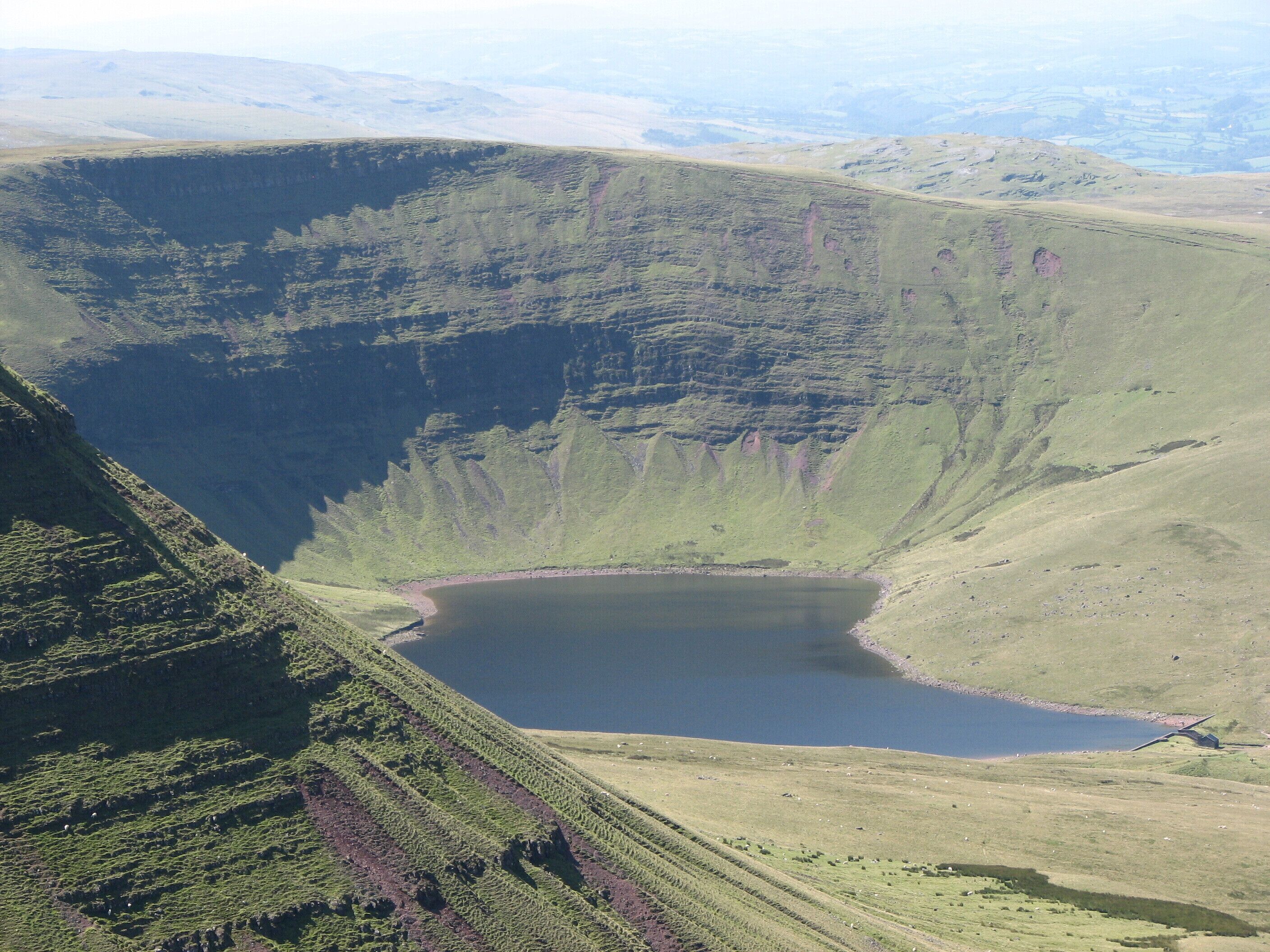 A large crater lake surrounded by green hills.