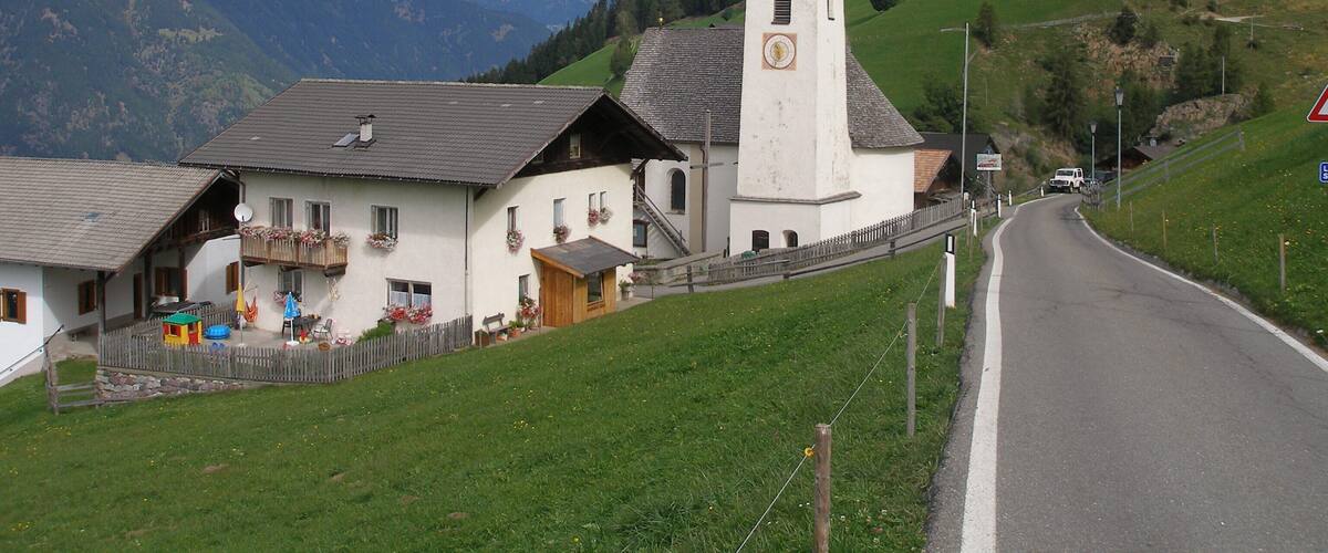 A white church with a clock tower, surrounded by green hills and mountains.