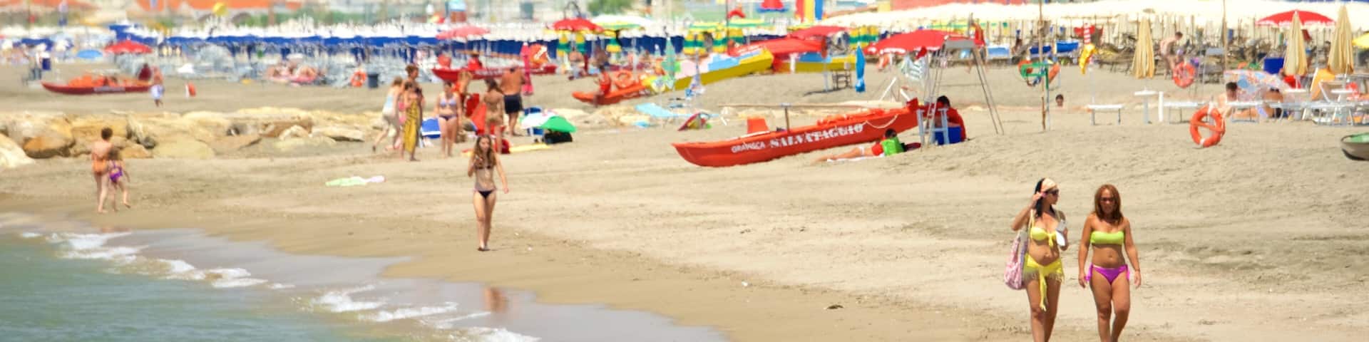 A crowded beach with people, umbrellas, and boats.