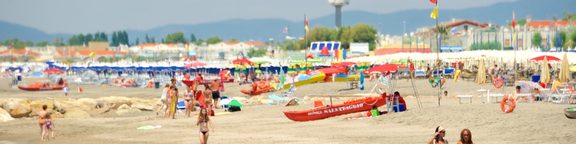 Una playa concurrida con gente, sombrillas y barcos.
