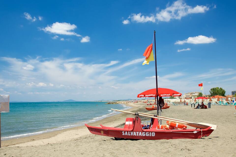 A beach with a lifeguard boat, umbrellas, and a clear blue sky.