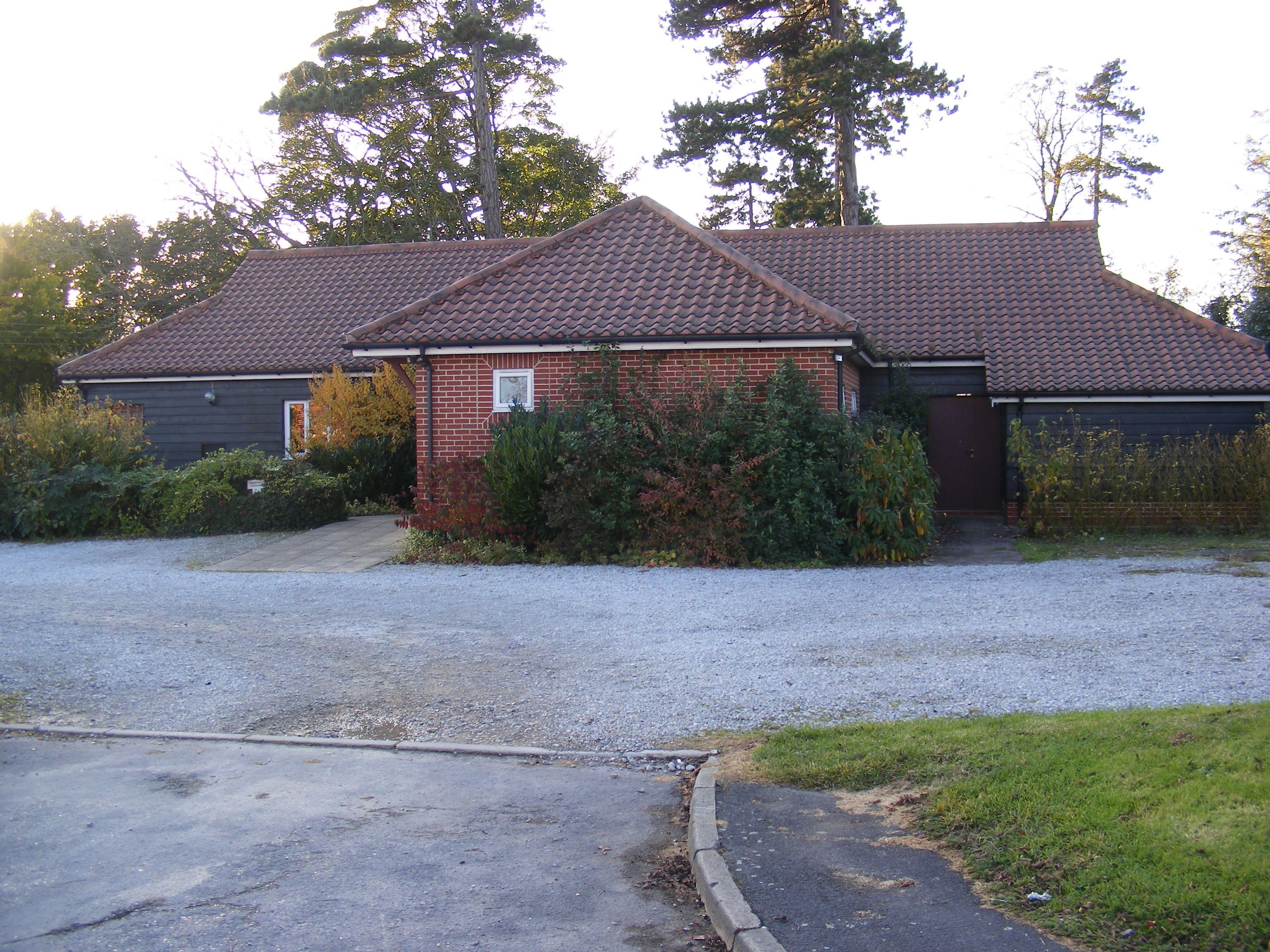 A two-story house with a tiled roof, surrounded by gravel driveway and dense shrubbery.