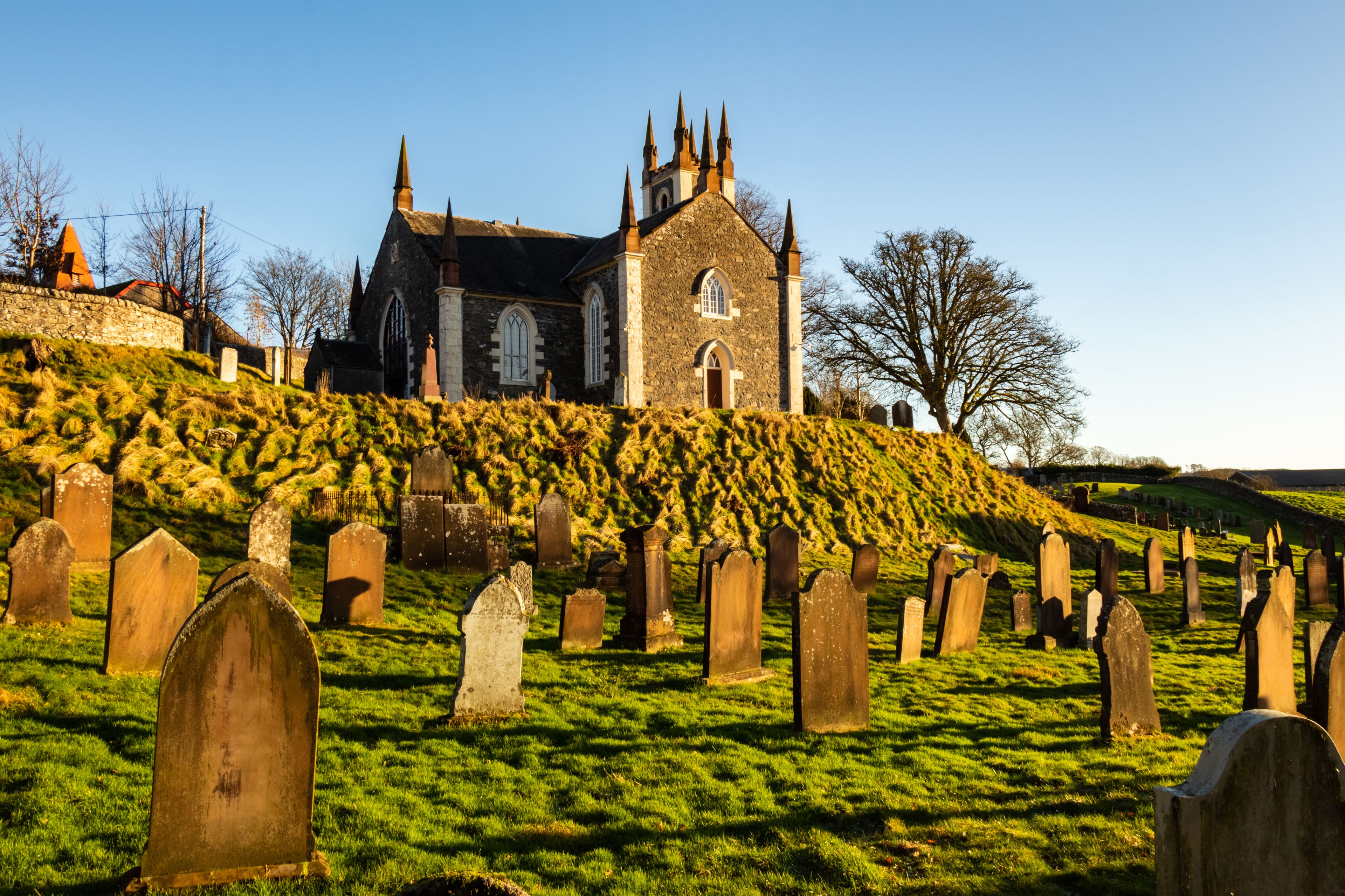 A church with a stone facade and multiple spires, surrounded by a cemetery with numerous headstones.