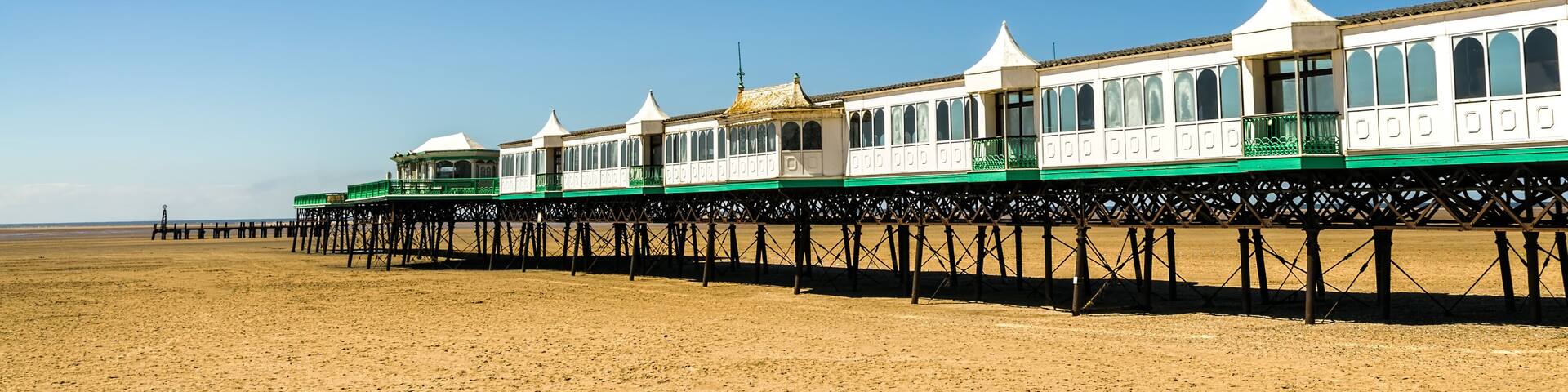 A beach with a row of white and green seaside houses on stilts.