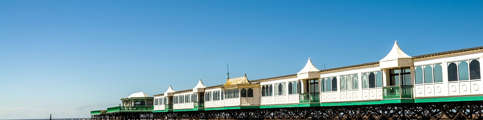 A beach with a row of white and green seaside houses on stilts.