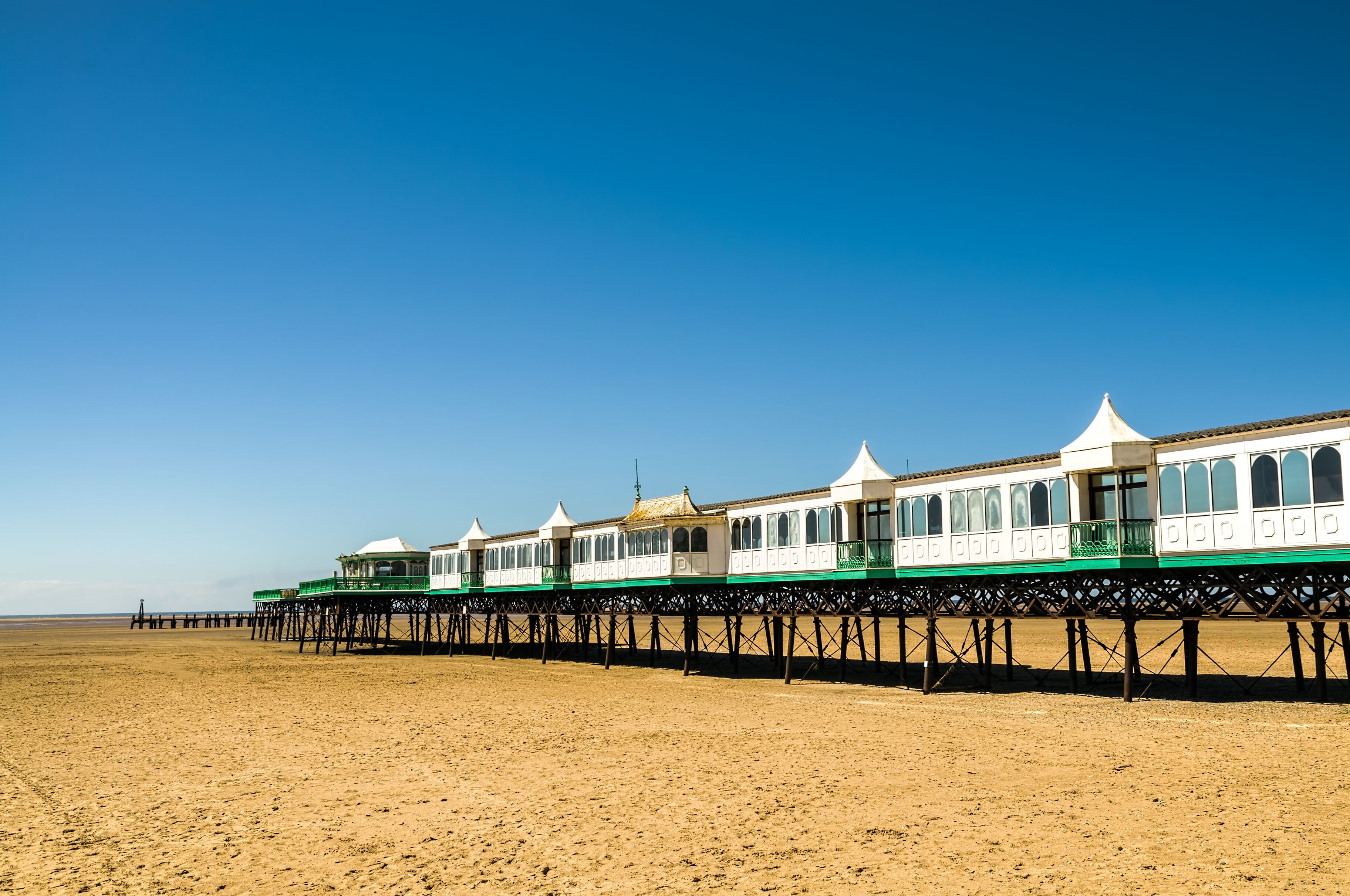 A beach with a row of white and green seaside houses on stilts.