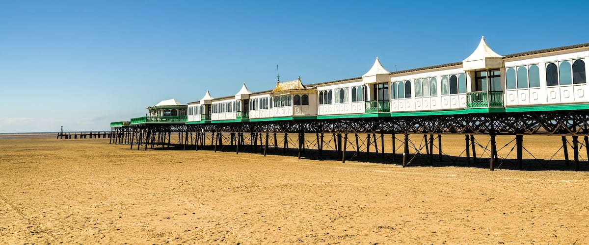 A beach with a row of white and green seaside houses on stilts.