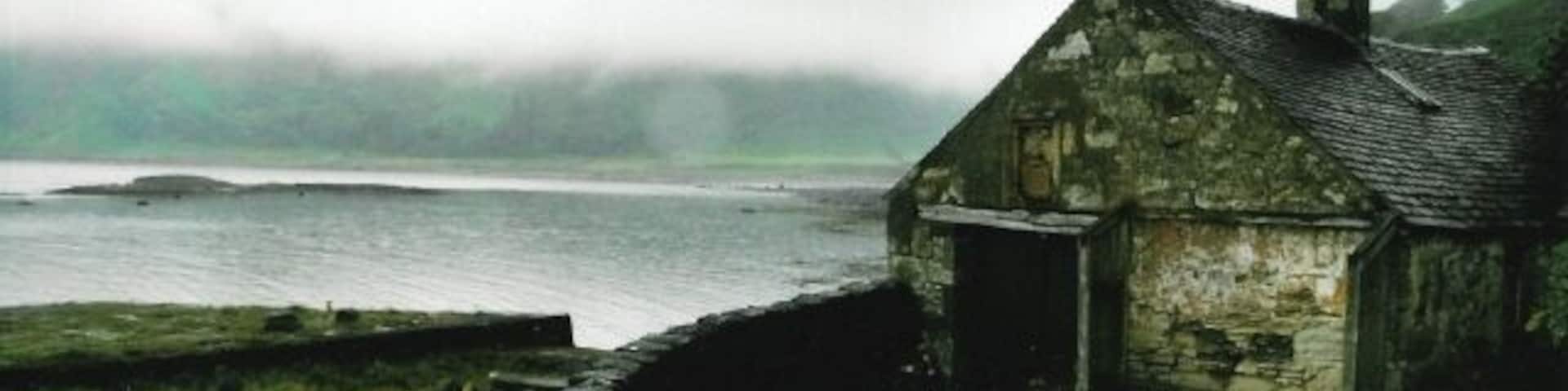 Boathouse at Carsaig Dilapidated but historic, the boathouse sports a find stone crest, allegedly moved from the 'big house' when the owner re-married. Low cloud obscures the cliffs on the other side of the bay.