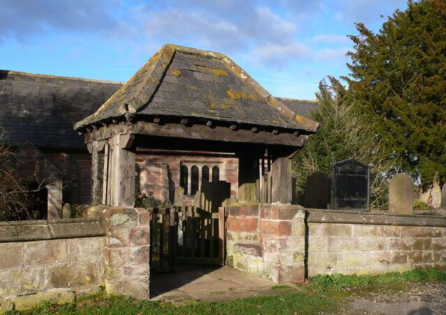 A small stone structure with a tiled roof, surrounded by a low stone wall and a grassy area.