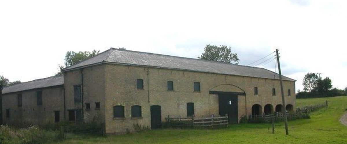 A large, old brick building with multiple windows and a central door, surrounded by a grassy field.