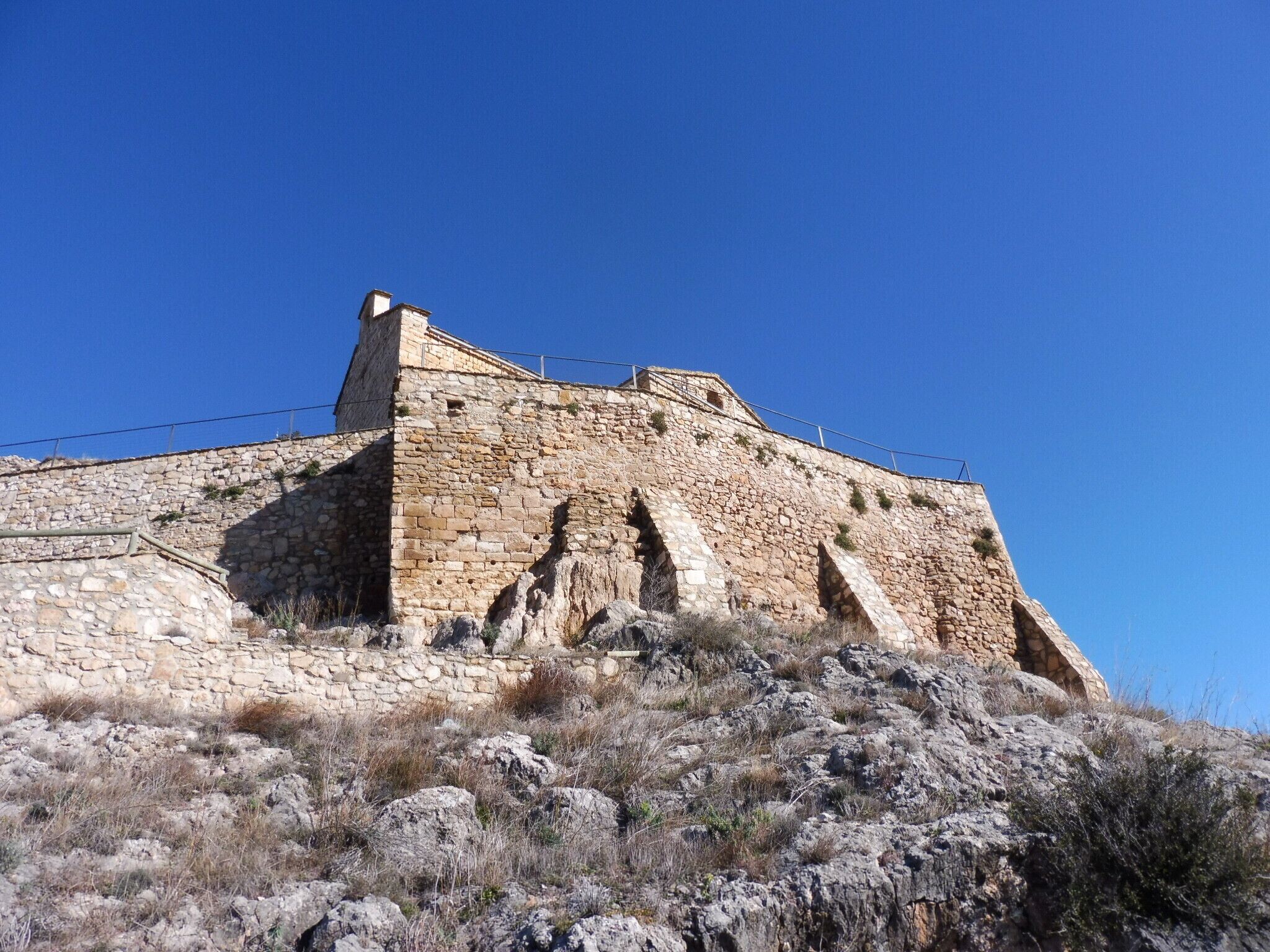 A stone fortification with a watchtower, surrounded by rocky terrain and sparse vegetation.