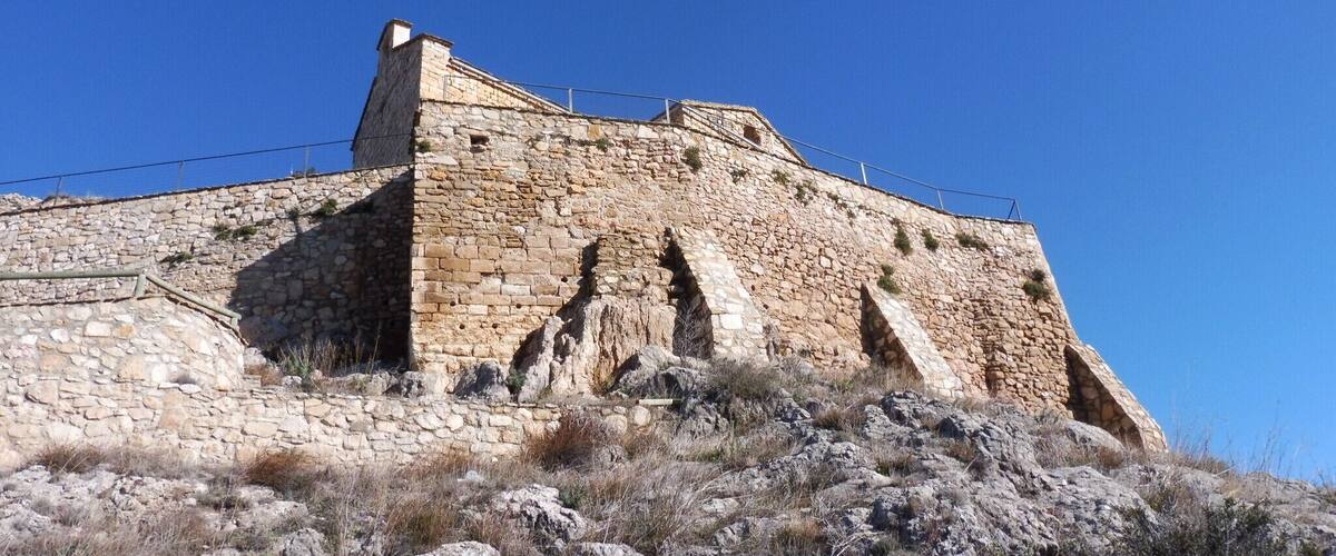 A stone fortification with a watchtower, surrounded by rocky terrain and sparse vegetation.