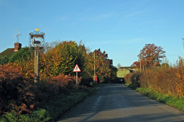A rural road with a warning sign, a blue signboard, and autumn foliage.