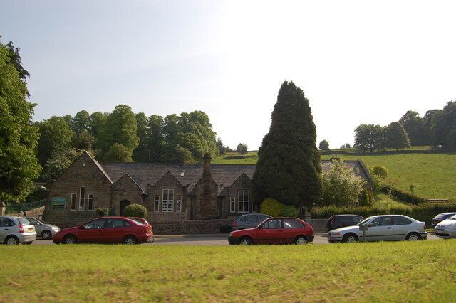 A building with a stone facade, parked cars, and a grassy field with trees.