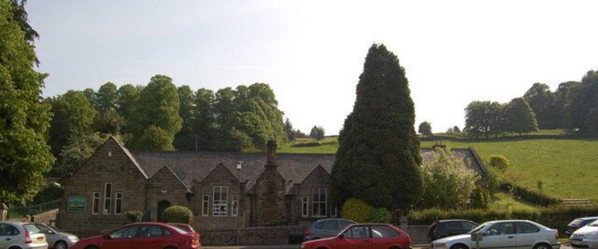 A building with a stone facade, parked cars, and a grassy field with trees.