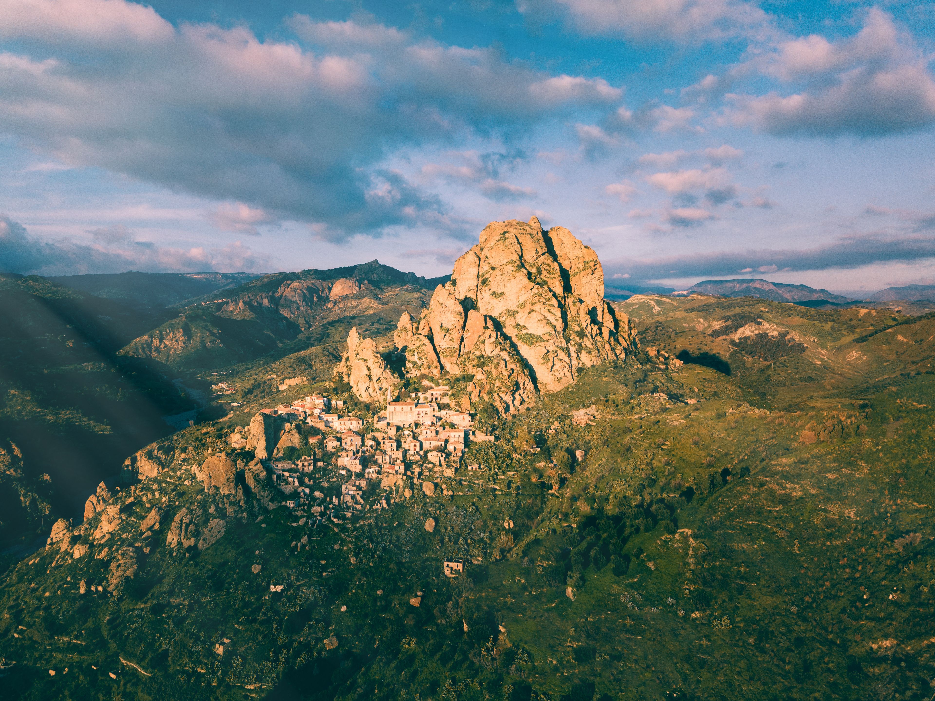 Un paisaje montañoso con una roca destacada y un pequeño pueblo enclavado entre las colinas.