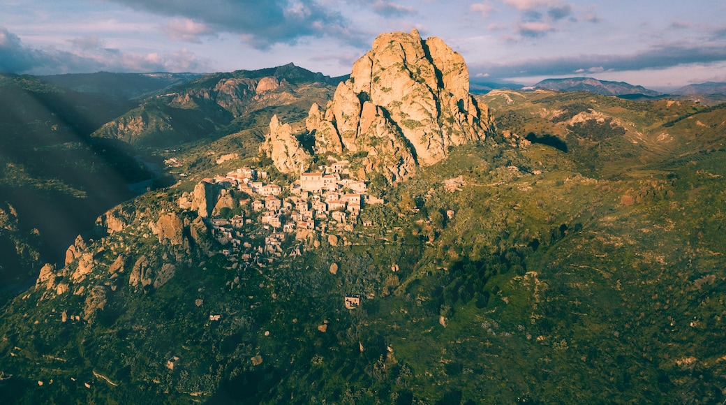 Un paisaje montañoso con una roca destacada y un pequeño pueblo enclavado entre las colinas.