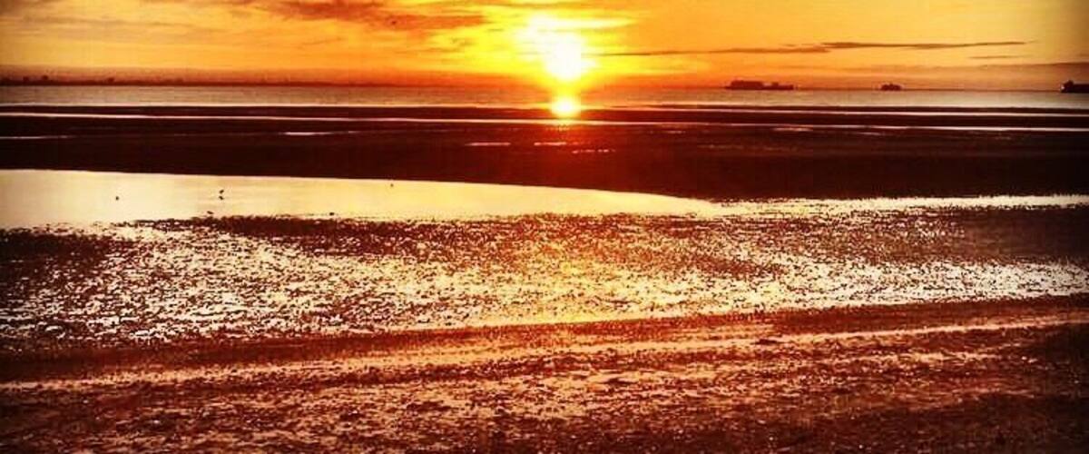 A sunset over a beach with clouds in the sky.