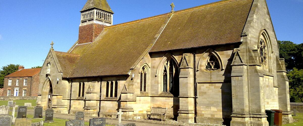A church with a tall steeple and a graveyard in front.
