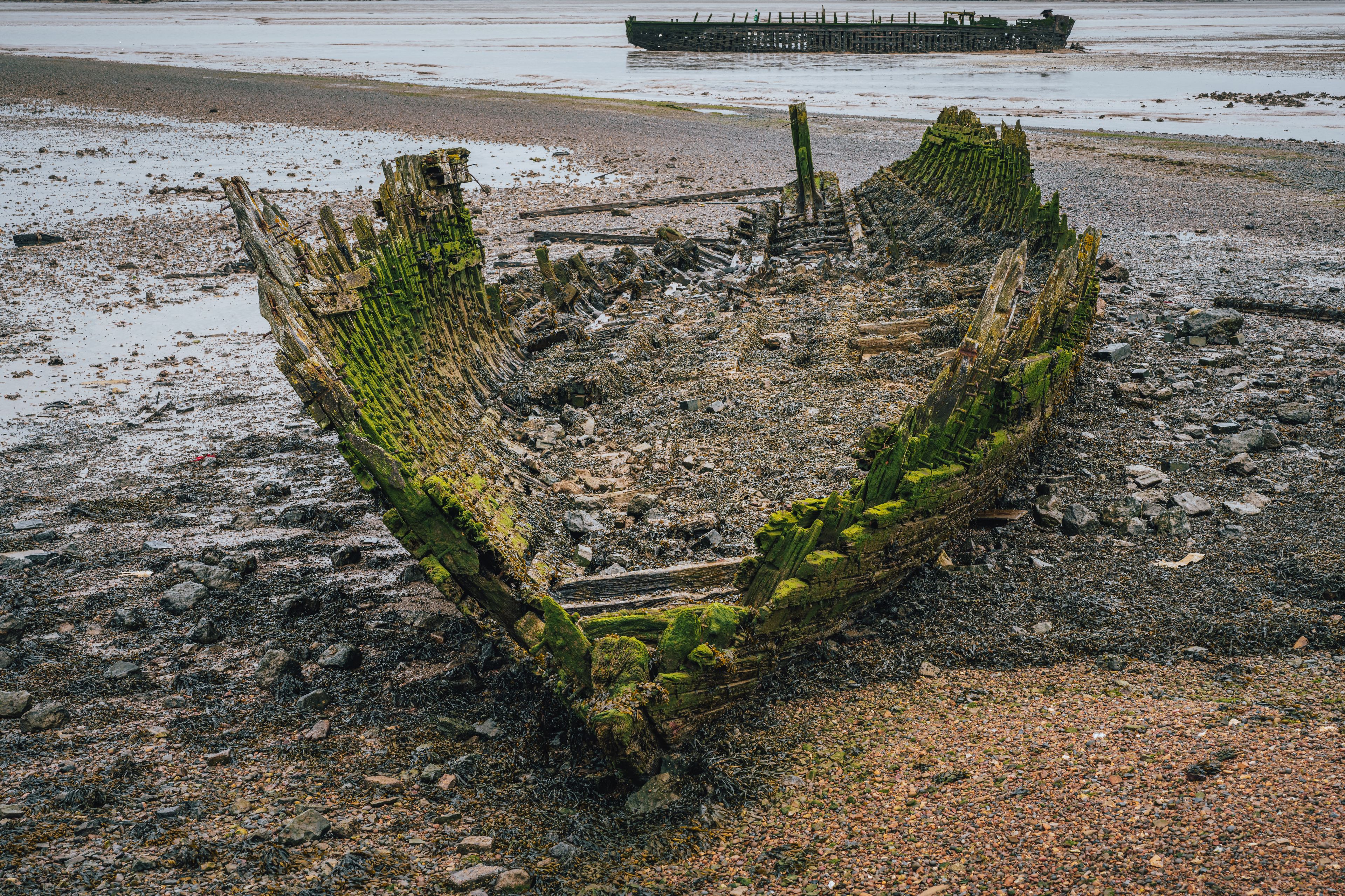 A shipwreck on a rocky shore with a large ship in the background.
