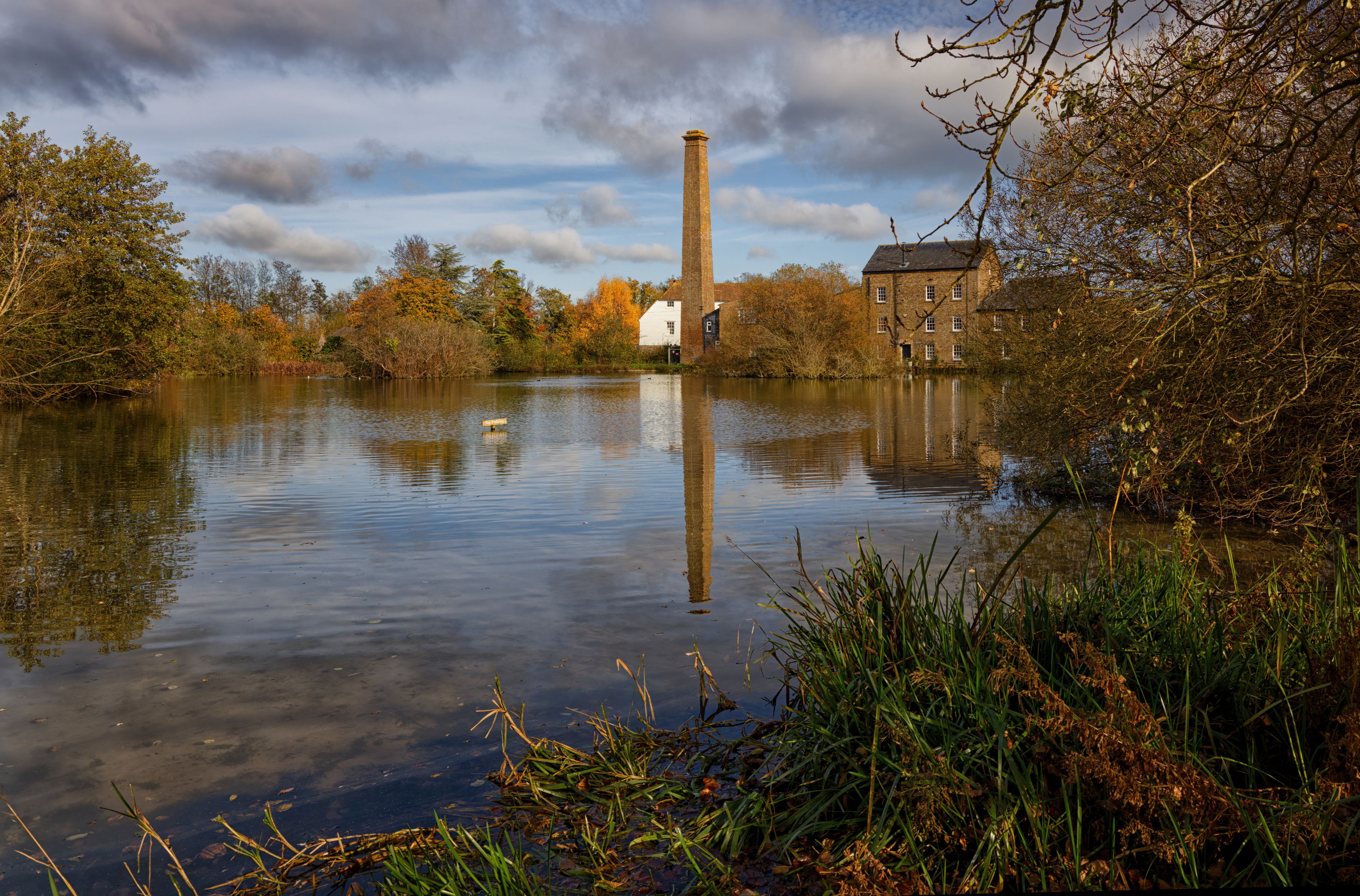 A calm river with a brick tower and a white building in the background.