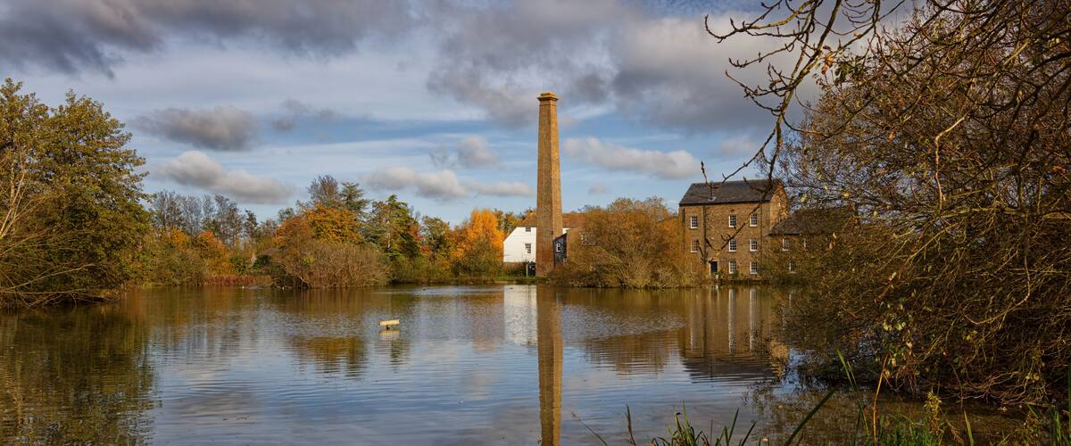 A calm river with a brick tower and a white building in the background.