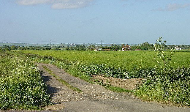 A rural road winding through green fields with distant buildings.