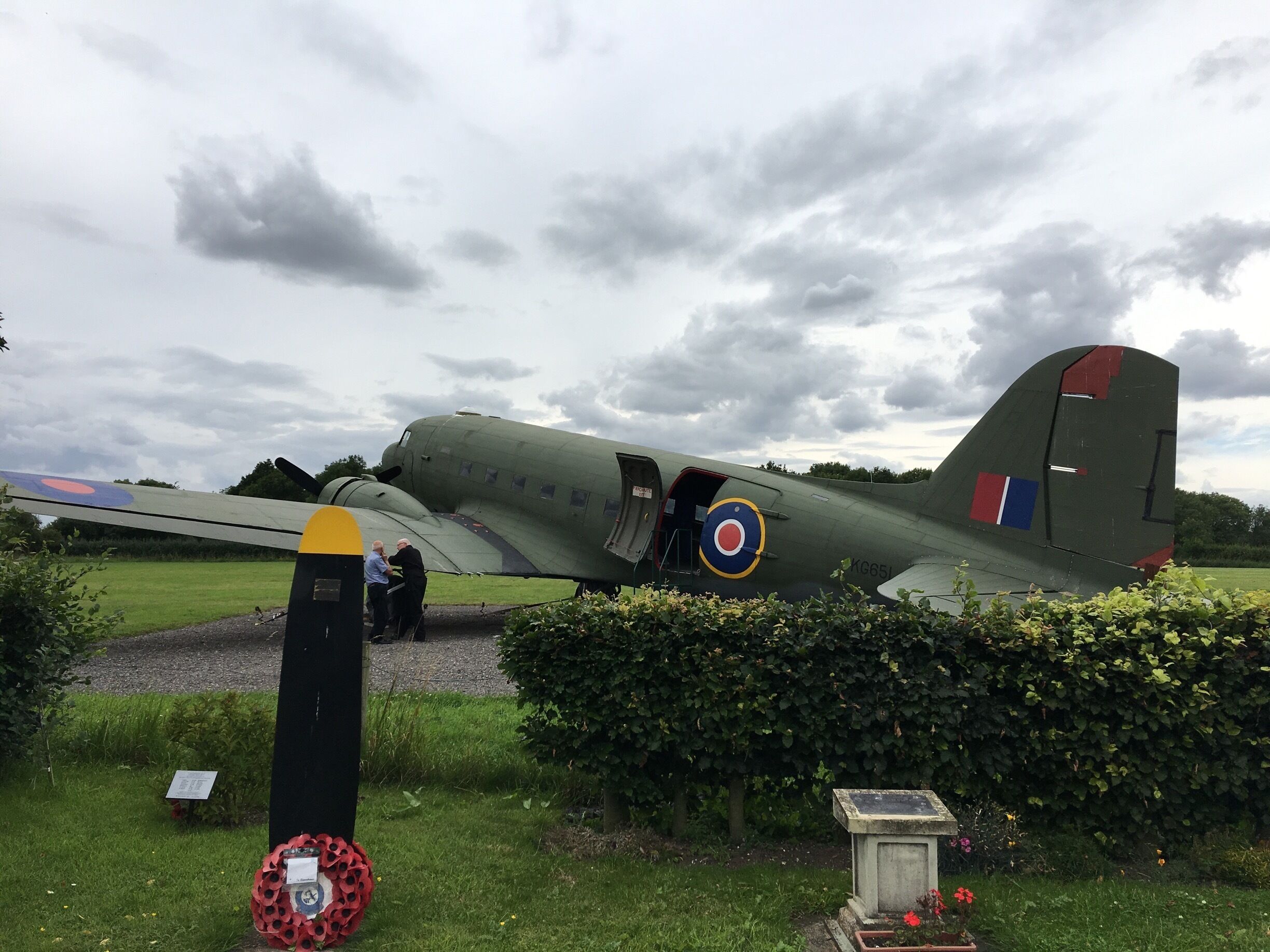 A vintage military aircraft on display with a grassy field and a hedge in the foreground.