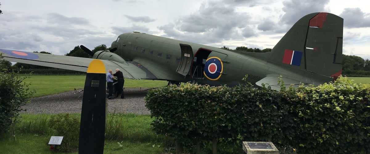 A vintage military aircraft on display with a grassy field and a hedge in the foreground.
