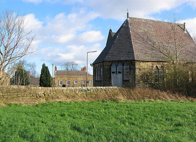 A stone building with a steep roof, surrounded by a stone wall and a grassy field.