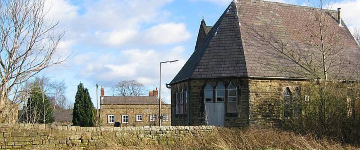 A stone building with a steep roof, surrounded by a stone wall and a grassy field.