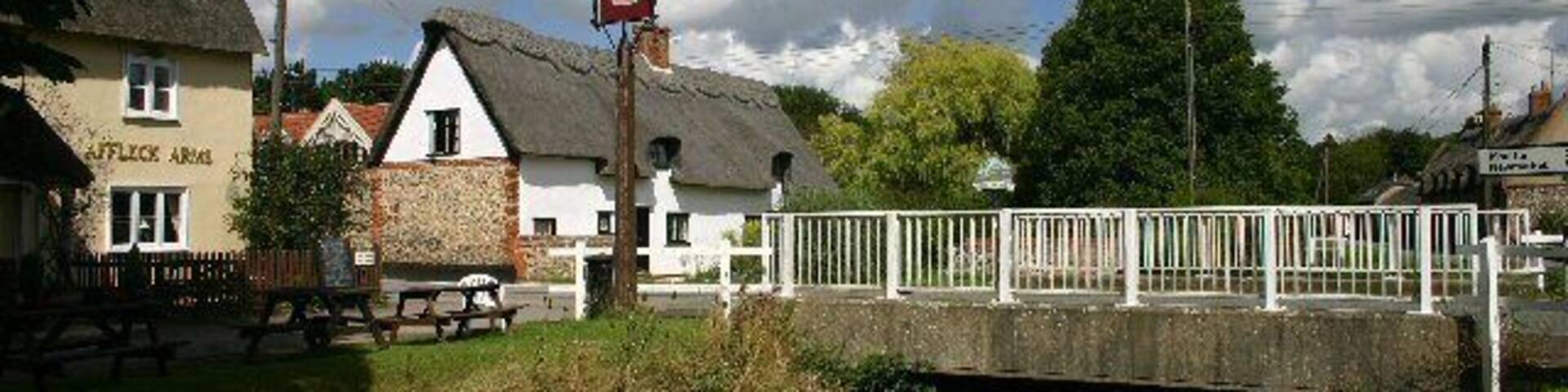 A bridge over a river, a pub named 'The Black Lion', and a thatched-roof building.