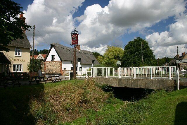 A bridge over a river, a pub named 'The Black Lion', and a thatched-roof building.