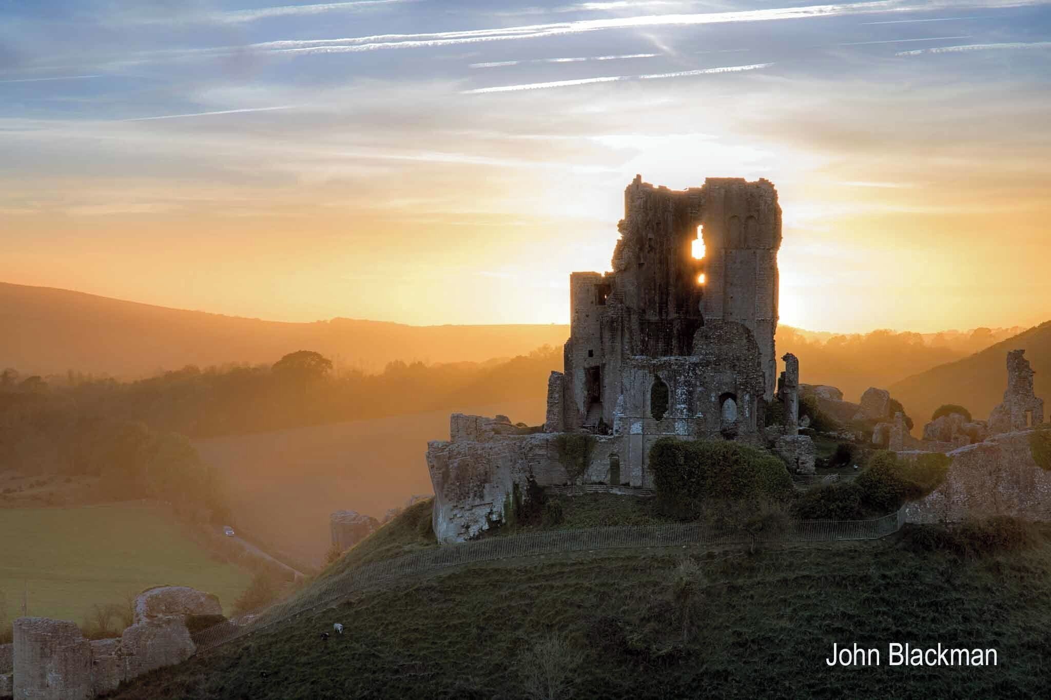 A historic castle ruin at sunrise with a clear sky.