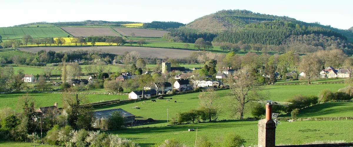 A rural landscape with rolling hills, fields, and scattered houses.