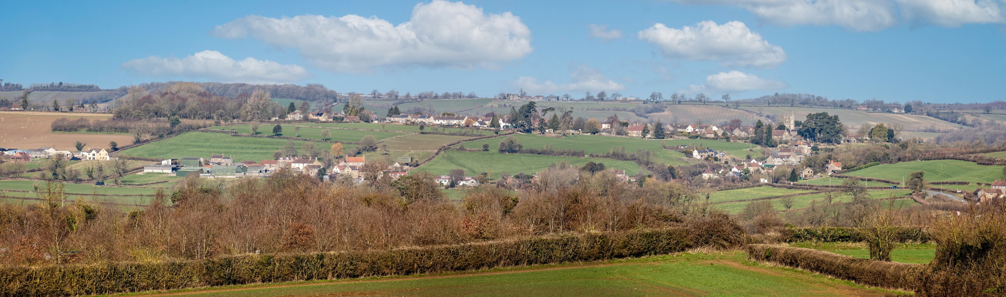 A rural landscape with rolling hills, scattered houses, and a prominent church tower.