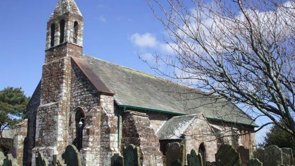 An old church with a bell tower and a green roof, surrounded by a cemetery.