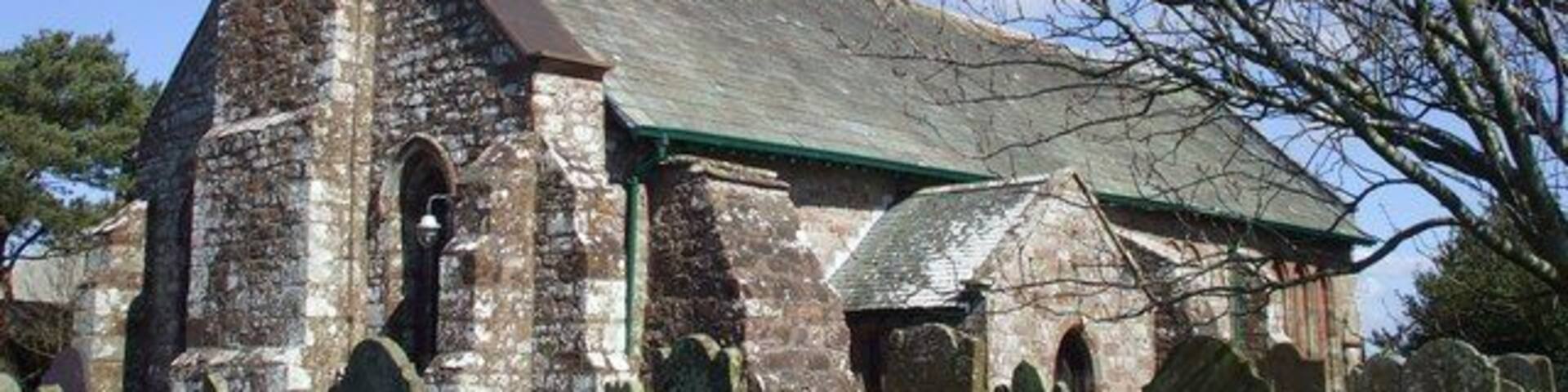 An old church with a bell tower and a green roof, surrounded by a cemetery.