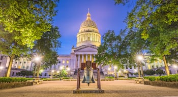 Das Kapitol von West Virginia im Abenddämmerung mit einer großen Glocke im Vordergrund.