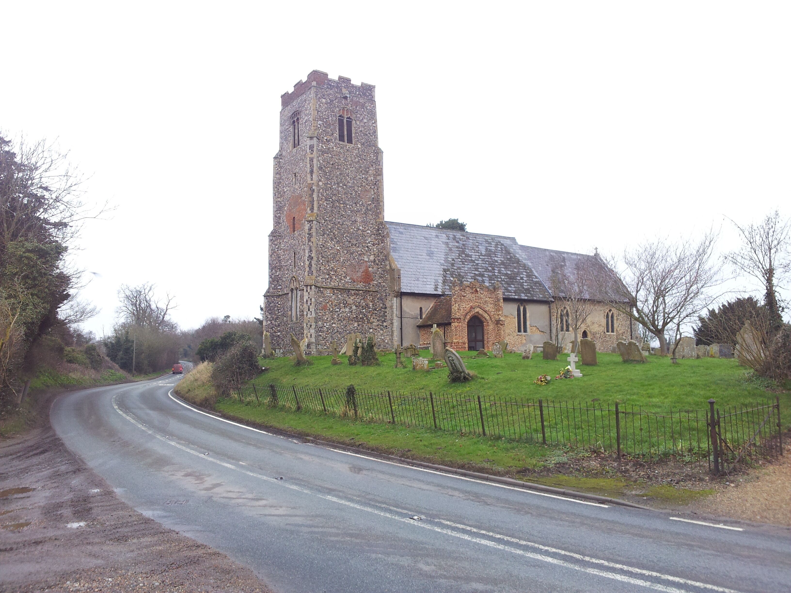 A stone church with a tall tower and a smaller building, surrounded by a fenced graveyard.