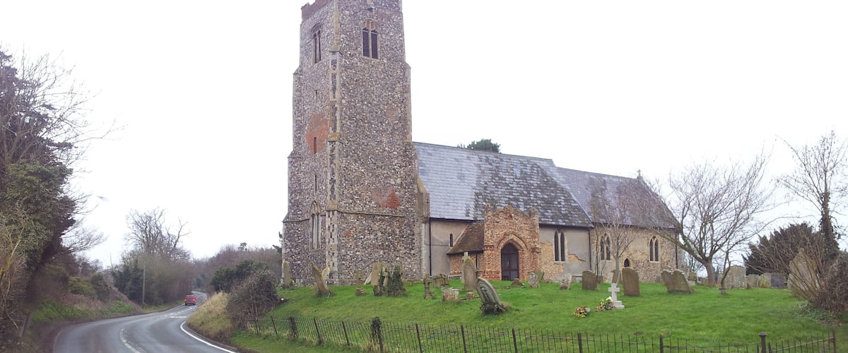 A stone church with a tall tower and a smaller building, surrounded by a fenced graveyard.