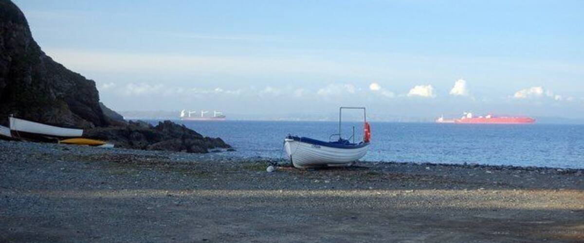 A rocky beach with a small boat and a distant ship.