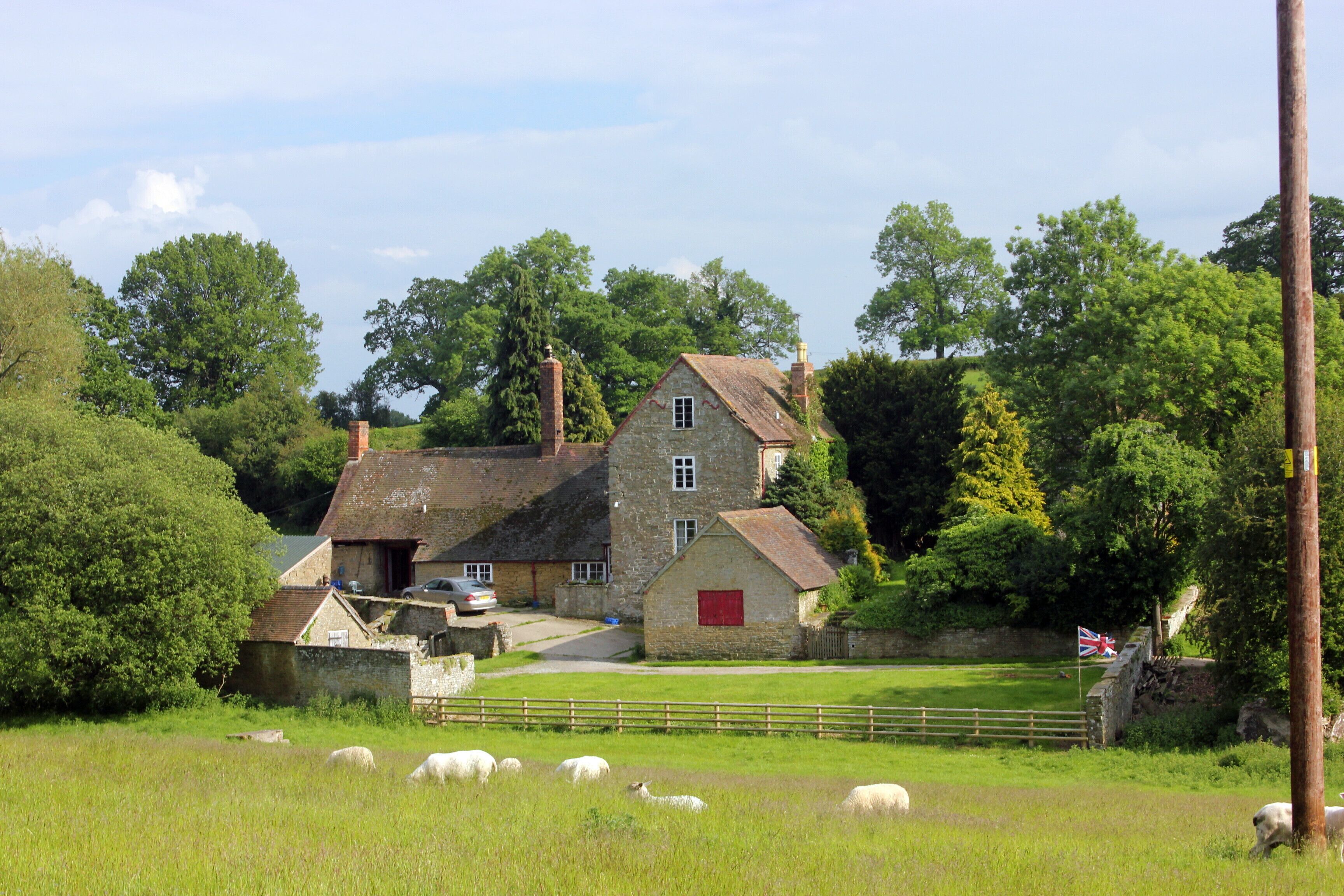A stone house with a red door, surrounded by a grassy field and sheep.