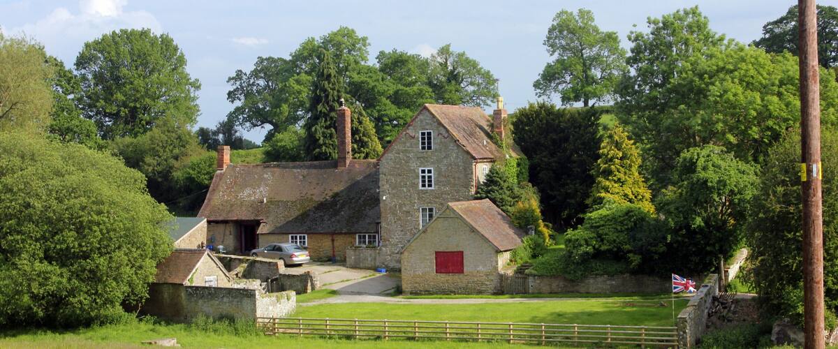 A stone house with a red door, surrounded by a grassy field and sheep.