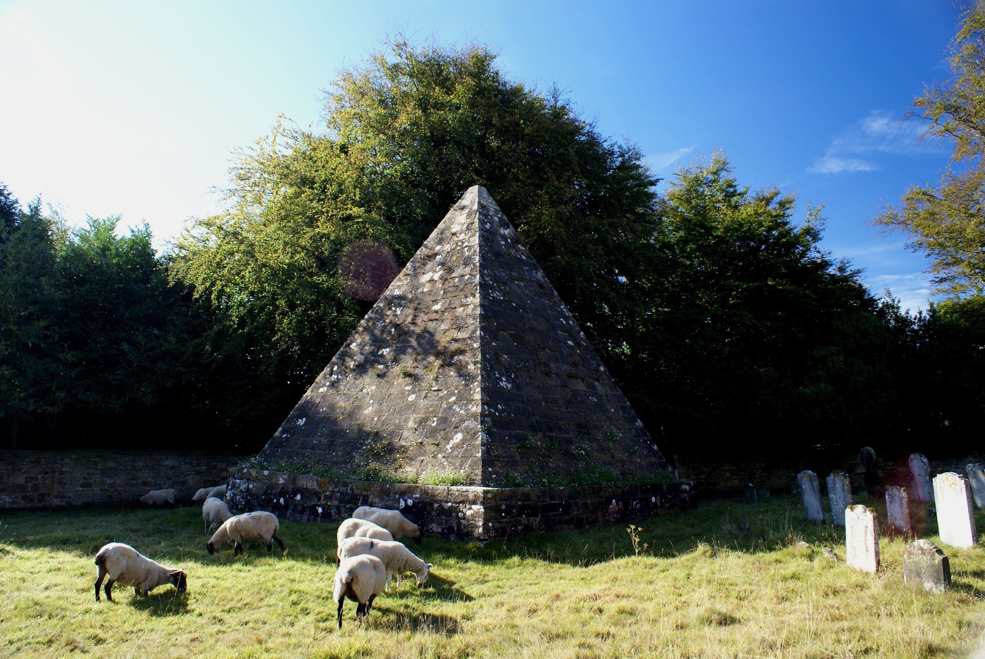 A pyramid-shaped monument surrounded by a grassy field and trees.