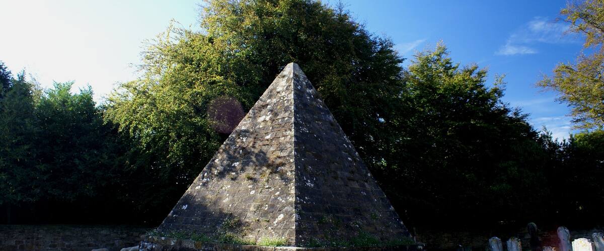 A pyramid-shaped monument surrounded by a grassy field and trees.