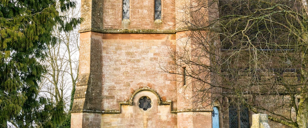 A historic stone tower with a pointed roof, arched windows, and a small bell tower.