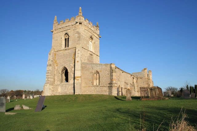 Tower and south aisle, St Mary's Church. Colston Bassett. This clearly shows the stages of the building of the tower. The early 13th century part is in rough blocks of blue lias limestone in thin courses. The later 15th century addition uses a facing of more substantial blocks of white limestone. The large grave on the right is that of Andrew Basilico who died in 1824 aged 79 years. His wife, Sophia Charlotte is also buried here. She died in 1850 aged 67. See 613460 for a brief history of the church.