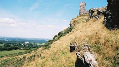 Uma torre de pedra numa colina verdejante sob um céu limpo.