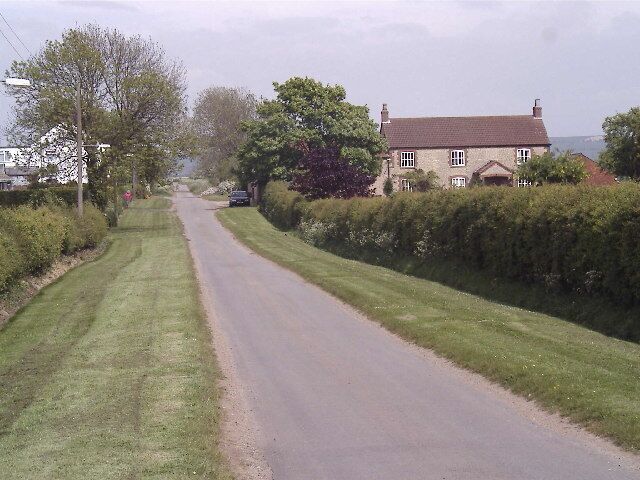 A rural road flanked by houses and greenery.